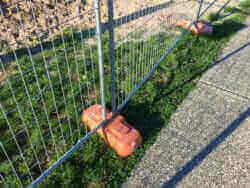A metal fence, used as temporary fencing, is next to a grassy area with Anti-Trip Support Blocks & Forks.